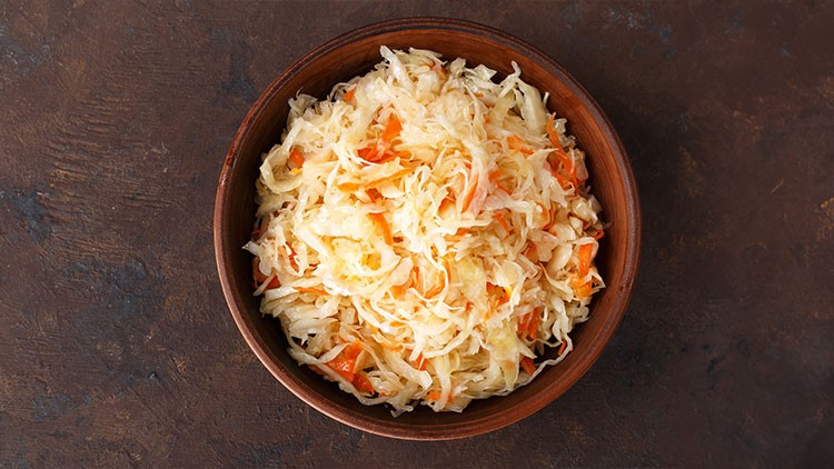 Ein brauner Teller mit frisch zubereitetem Sauerkraut und feinen Karottenstreifen auf dunklem Untergrund.