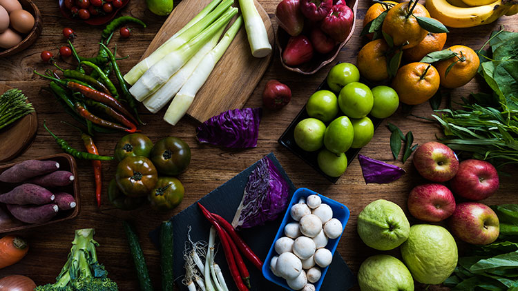 Verschiedenes Obst und Gemüse wie Äpfel, Paprika, Lauch, Champignons und Rotkohl auf einem Holztisch angeordnet.