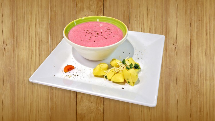 Auf einem weißen Teller stehen eine rosa Suppe in einer Schale und gelbe Kartoffeln mit Kräutern, Käse und einer Tomatenscheibe.