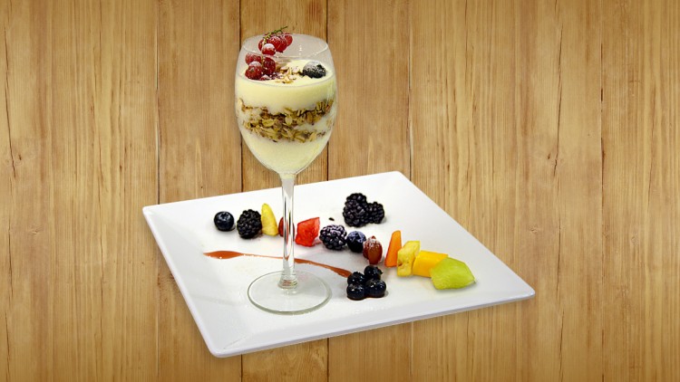 Ein Dessert im Weinglas mit Schichten aus Joghurt und Müsli, dekoriert mit Beeren, auf einem Teller mit Obst und Fruchtsoße.