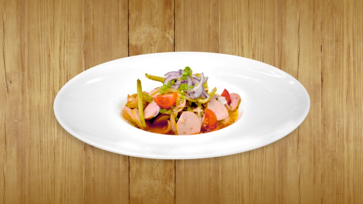 Ein weißer Teller mit Wurstsalat aus Gemüse, roten Zwiebeln, Kirschtomaten und Dressing auf Holzuntergrund.