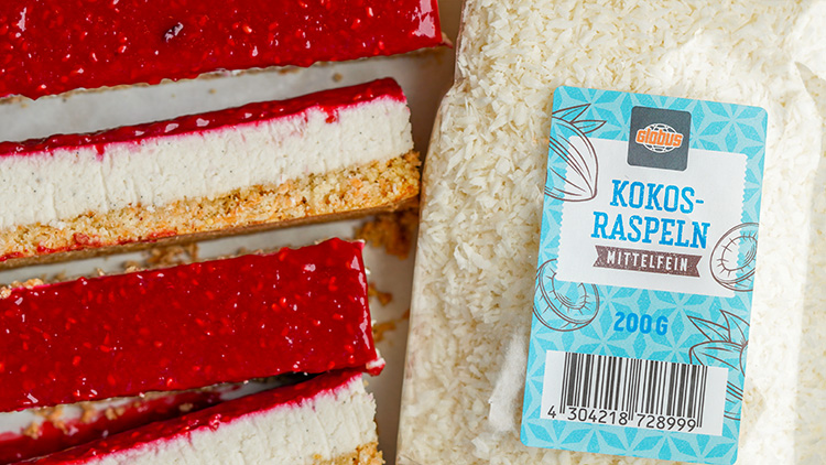 Rote Kuchenstücke mit heller Creme auf Keksboden liegen neben einer 200g-Packung GLOBUS Kokosraspeln, mittelfein.