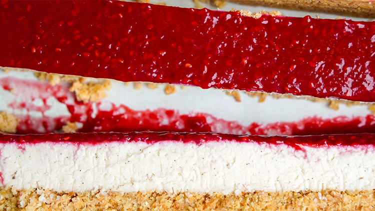 Quarkkuchen mit rotem Himbeerbelag und knusprigem Boden aus Kekskrümeln, Schichtung von oben nach unten sichtbar.