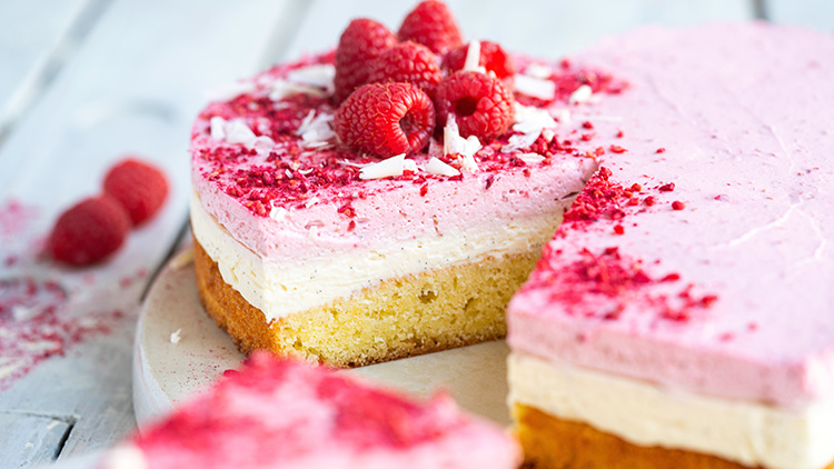 Eine angeschnittene Himbeercremetorte mit weißer Schicht, dekoriert mit frischen Himbeeren und weißen Schokoraspeln.