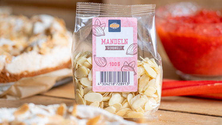 Transparente Verpackung mit 100 g gehobelten Mandeln und GLOBUS-Logo, im Hintergrund Kuchen und rote Fruchtsoße.