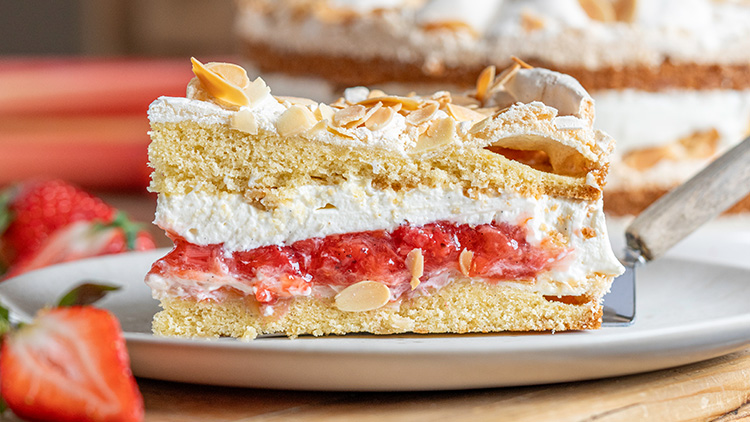 Ein Stück Sahnetorte mit Erdbeerschicht, Mandelblättchen und heller Creme auf einem Teller mit frischen Erdbeeren.