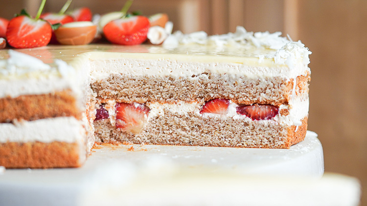 Anschnitt einer Sahnetorte mit braunem Biskuitteig, frischen Erdbeeren und weißer Dekoration aus Sahne und Schokolade.