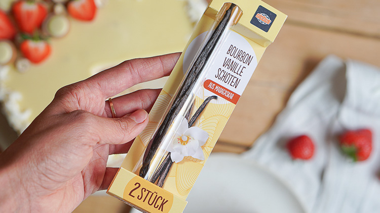 Eine Hand hält eine Packung mit der Aufschrift „Bourbon Vanille Schoten aus Madagaskar, 2 Stück“ in gelbem Design.