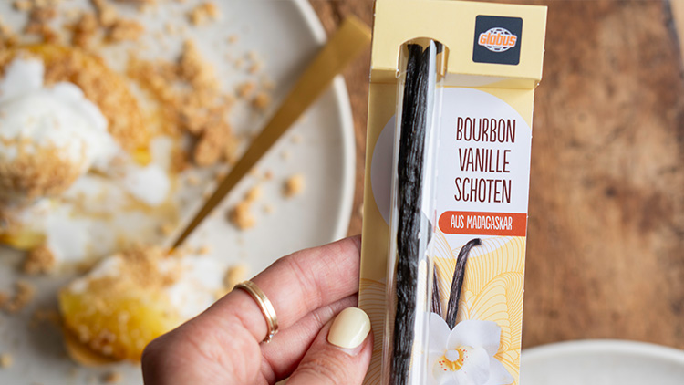 Packung mit Bourbon-Vanilleschoten von GLOBUS aus Madagaskar, daneben ein Teller mit Dessert und goldenem Besteck.