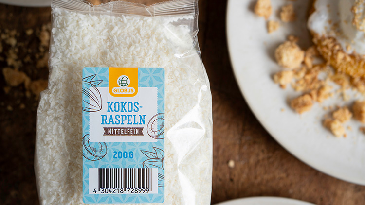Eine Packung GLOBUS Kokosraspeln mit blauem Etikett und der Aufschrift „Kokosraspeln, mittelfein, 200 g“ liegt neben zwei Tellern.