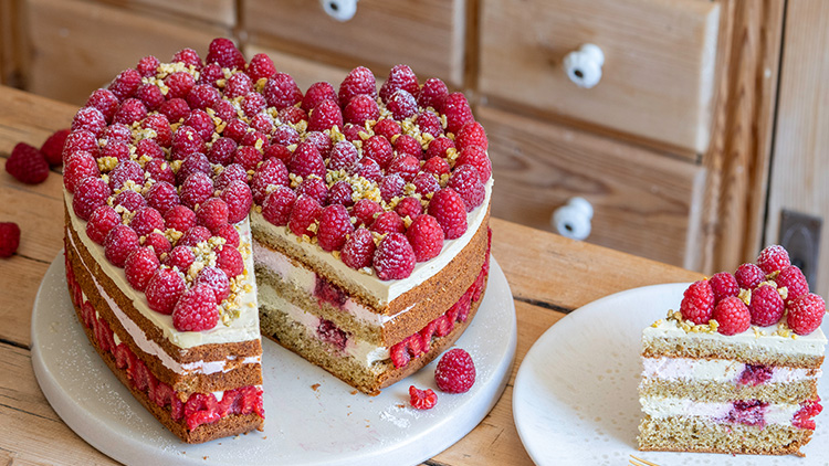 Runde Himbeertorte mit mehreren Schichten, Sahnefüllung und Dekoration aus frischen Himbeeren und gehackten Pistazien.