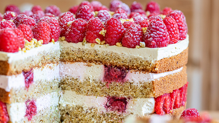 Mehrschichtige Torte mit heller Creme, Himbeeren und goldenen Streuseln, im Anschnitt mit sichtbar eingebetteten Himbeeren.