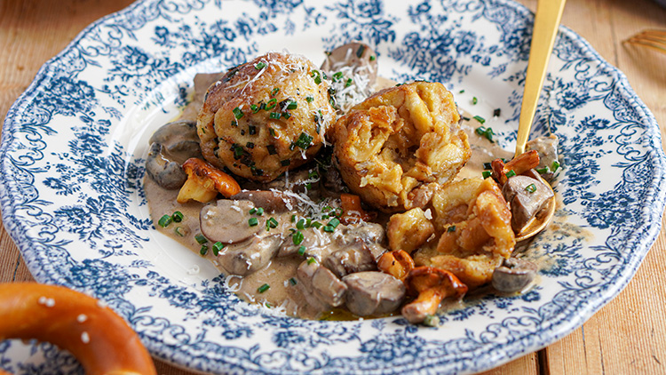 Zwei Semmelknödel auf Rahmsauce mit Pilzen wie Champignons und Pfifferlingen, dekoriert mit Schnittlauchröllchen.