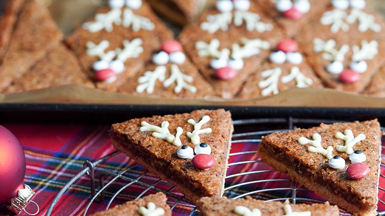 Dreieckige Lebkuchenstücke mit Zuckerdekoration, Augen, roter Nase und weißen Geweihen auf Tablett und Gitter.