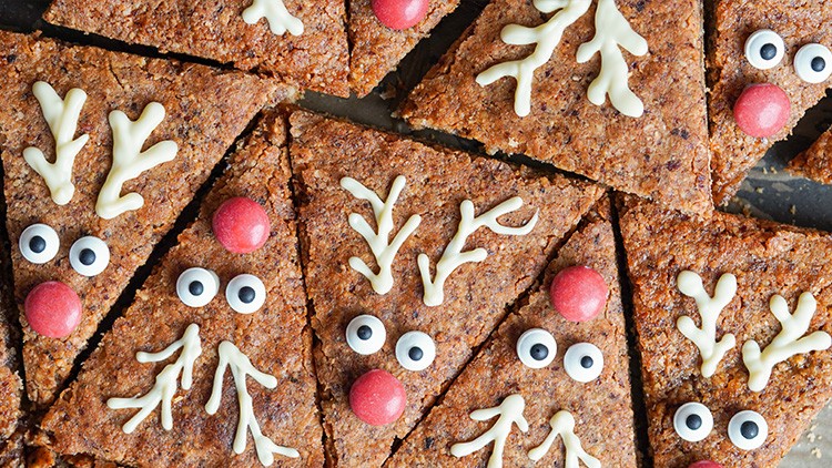 Dreieckige Kekse mit weißen Schokoladengeweihen, Zuckeraugen und roten Nasen, dekoriert im Rentierdesign.