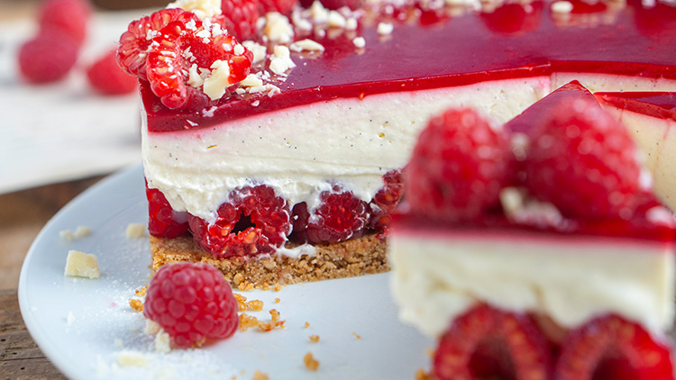 Himbeer-Cremetorte mit roter Gelee-Schicht, weißer Creme, Mandelsplittern und frischen Himbeeren auf einem Teller.