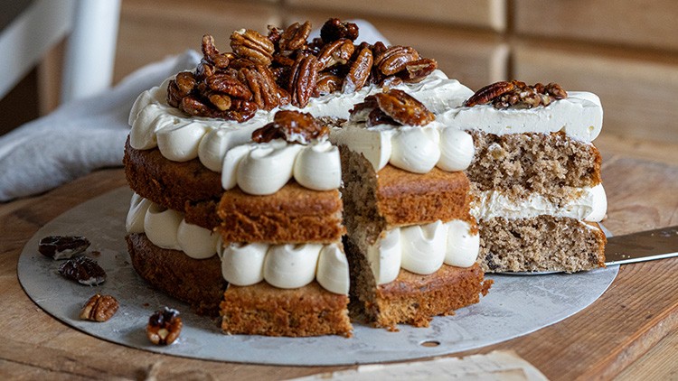 Nusskuchen mit zwei Schichten und Cremefüllung, dekoriert mit ganzen Pekannüssen, ein Stück ist angeschnitten.