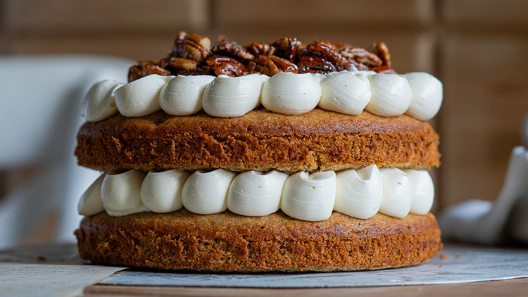 Zweistöckiger Kuchen mit weißer Creme zwischen den Schichten und gebrannten Nüssen als Dekoration auf der Oberseite.