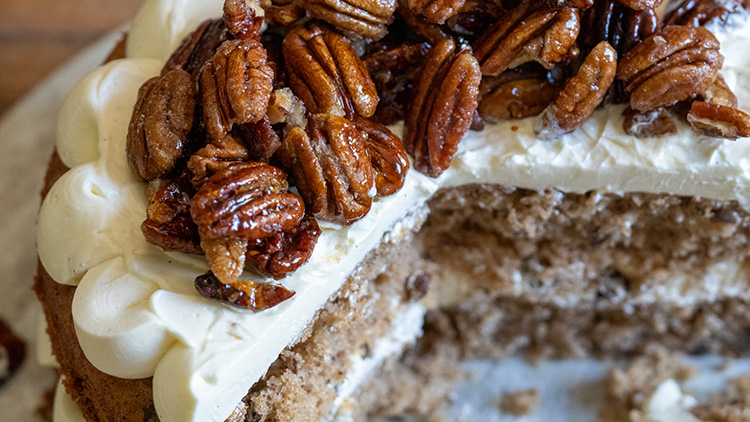 Anschnitt einer Sahnetorte mit karamellisierten Pekannüssen als Dekoration auf der Oberfläche.
