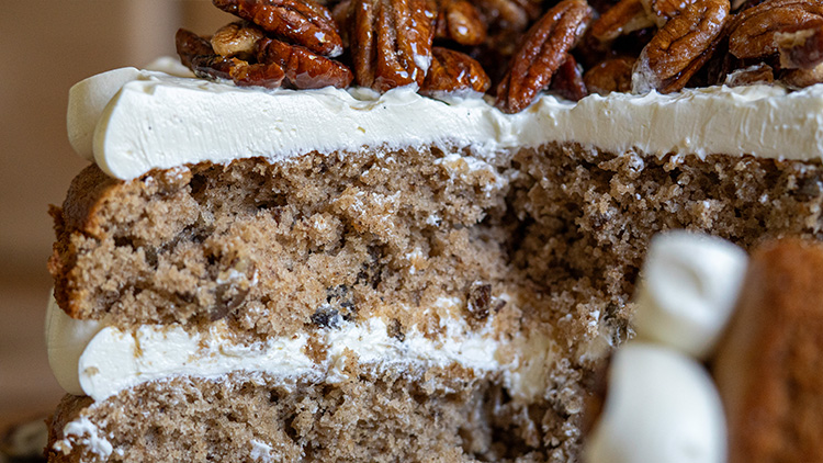 Anschnitt eines zweischichtigen Kuchens mit heller Cremefüllung und Zuckerguss, dekoriert mit karamellisierten Pekannüssen.