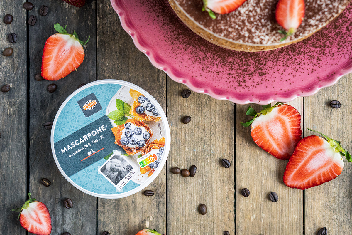 Runde Mascarpone-Packung von GLOBUS mit Beeren-Dekor, Erdbeeren, Kaffeebohnen und Kuchen auf Holzuntergrund.