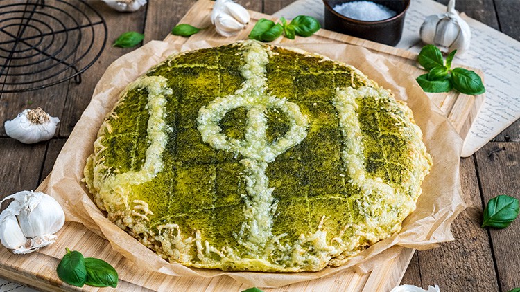 Eine grüne Focaccia mit Knoblauch liegt auf Backpapier, umgeben von frischem Basilikum, Knoblauchknollen und Salz.