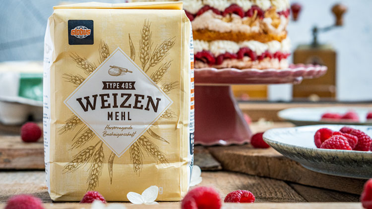 Eine Packung GLOBUS Weizenmehl Type 405 steht auf einem Tisch mit Himbeeren und einer Torte im Hintergrund.