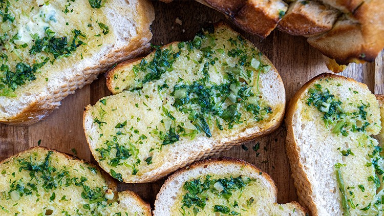 Geröstete Brotscheiben mit Kräuterbutter und fein gehackten, frischen Kräutern auf einer Holzunterlage.