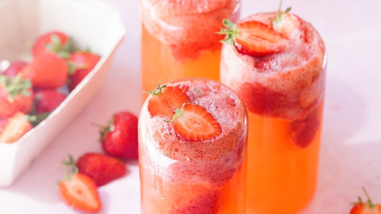 Drei Gläser mit rotem Erdbeergetränk und frischen Erdbeerscheiben, daneben liegen Erdbeeren und eine weiße Schale.