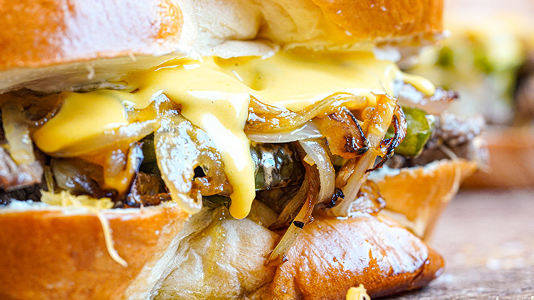 Nahaufnahme eines Burgers mit geschmolzenem Käse, gebratenen Zwiebeln und Brötchen mit glänzender, goldbrauner Kruste.