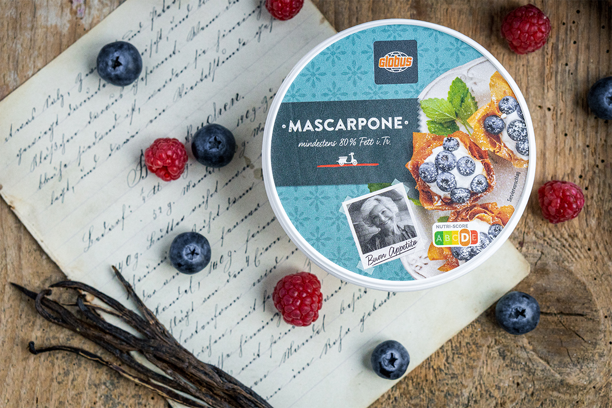 Runde Mascarpone-Verpackung von GLOBUS auf Holzuntergrund mit Himbeeren, Blaubeeren, Vanilleschoten und handgeschriebenem Rezept.