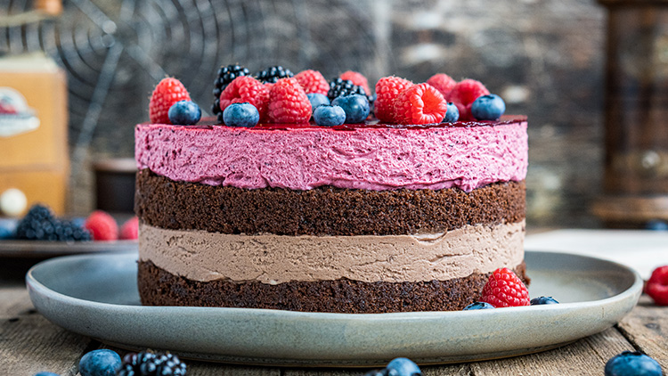 Torte mit drei Schichten aus Schokoladenböden, rosa und brauner Creme, dekoriert mit Himbeeren, Brombeeren und Blaubeeren.