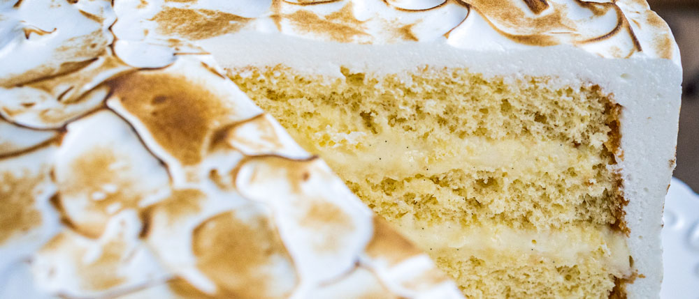 Anschnitt einer hellen, zweischichtigen Torte mit gelber Cremefüllung und leicht gebräunter Baiser-Deckschicht.