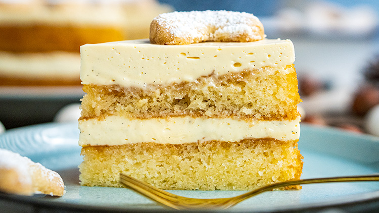 Ein Stück heller Schichtkuchen mit zwei Cremeschichten und einem mit Puderzucker bestreuten Gebäck oben auf türkisem Teller.