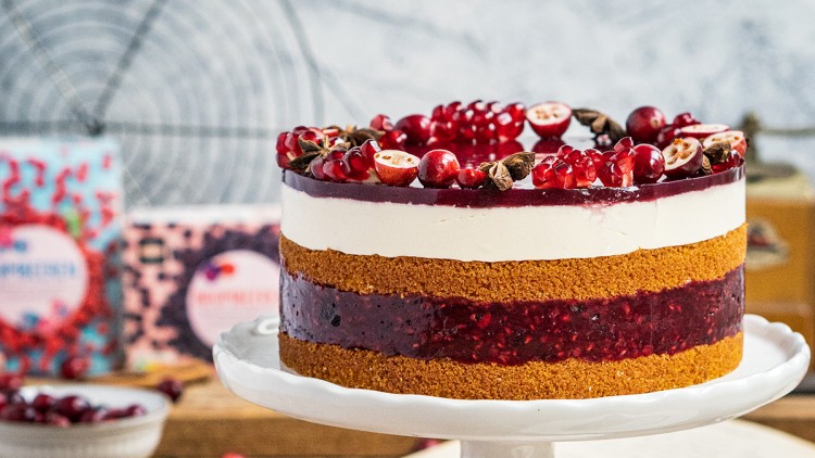 Schichttorte mit roter Fruchtschicht und Sahneschicht auf weißer Tortenplatte, dekoriert mit roten Beeren und Sternanis.