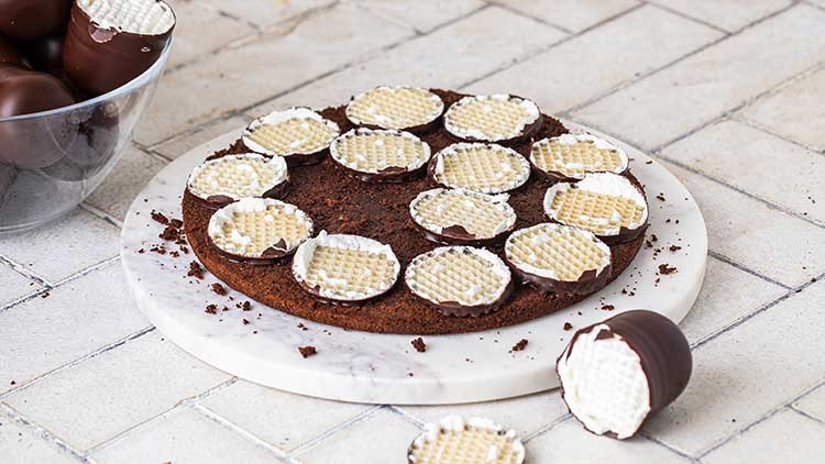 Runder Schokoladenkuchen auf weißem Teller, belegt mit halbierten Schokoküssen, daneben eine Schale mit weiteren Schokoküssen.