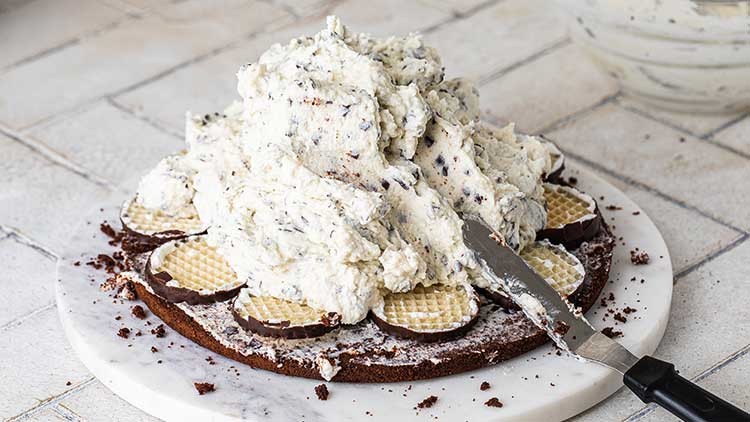 Ein dunkler Tortenboden mit Schokowaffeln darauf, bedeckt von heller Sahnecreme mit Schokostückchen, daneben ein Messer.