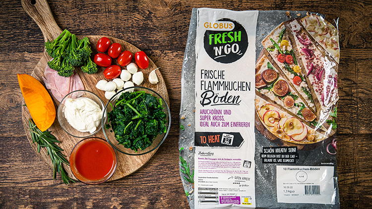 Auf einem Holztisch liegen Zutaten für Flammkuchen und eine Packung GLOBUS Fresh N´Go Flammkuchen-Böden.