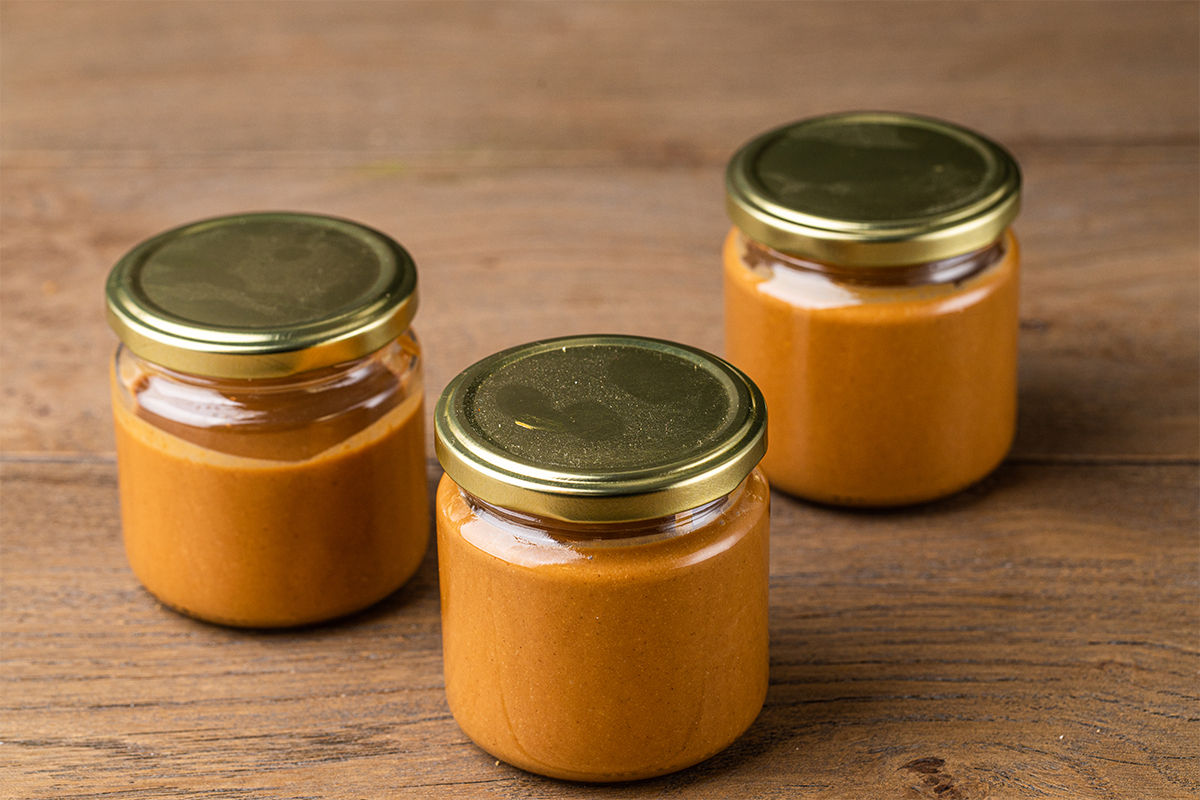 Drei kleine, mit orangefarbener Creme gefüllte Glasbehälter mit goldfarbenen Deckeln stehen auf einer Holzoberfläche.