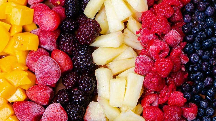 Gefrorene Mango, Erdbeeren, Brombeeren, Ananas, Himbeeren und Blaubeeren liegen in Streifen dicht nebeneinander.