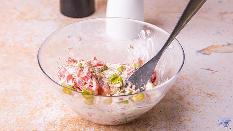 Glasschüssel mit Tomatensalat, Frühlingszwiebeln und cremigem Dressing, darin ein Metalllöffel, Salz- und Pfefferstreuer im Hintergrund.