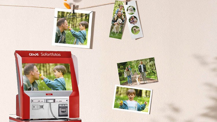 Ein roter CEWE Sofortfotos-Automat steht vor einer Wand mit aufgehängten Fotografien.