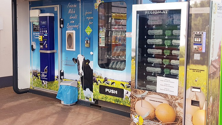 Automat für frische Milch, Eier und regionale Produkte mit Kuhmotiv und der Aufschrift „Frische Milch direkt vom Bauernhof“.