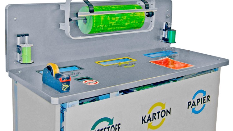 Abfalltrennstation mit Einwurfschächten für Kunststoff, Karton und Papier sowie Rollen für Klebeband und grüne Folie.