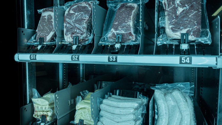 Verpackte Fleischstücke, gefüllte Nudelteigtaschen und Bratwürste in einem nummerierten Warenregal eines Automaten.