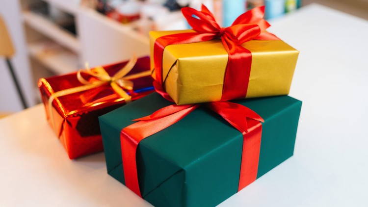 Drei bunt verpackte Geschenke mit roten Schleifen liegen auf einer weißen Tischplatte.