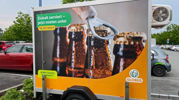 Anhänger mit Werbung zeigt Bierflaschen, einen Flaschenöffner und Text „Eiskalt serviert – jetzt mieten unter Tel. 0371 69573-0“.