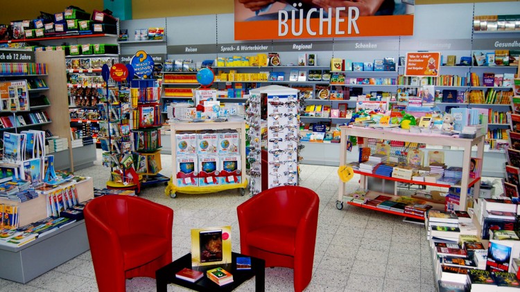 Bereich mit Bücherregalen, zwei roten Sesseln, einem schwarzen Tisch mit Büchern und einem Schild mit „BÜCHER“ an der Wand.