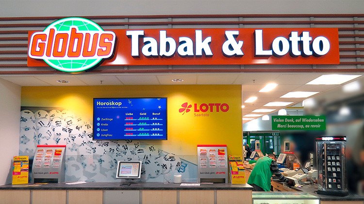 Der GLOBUS Tabak & Lotto-Bereich mit gelber Wand, Display mit Horoskop und Lotto Saarloto-Logo, Verkaufsregale und Infotafel.