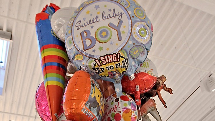 Ein Bündel bunter Ballons, einer trägt den Text „Sweet baby BOY“ und „I SING! TAP TO PLAY“, in einem Innenraum mit heller Decke.